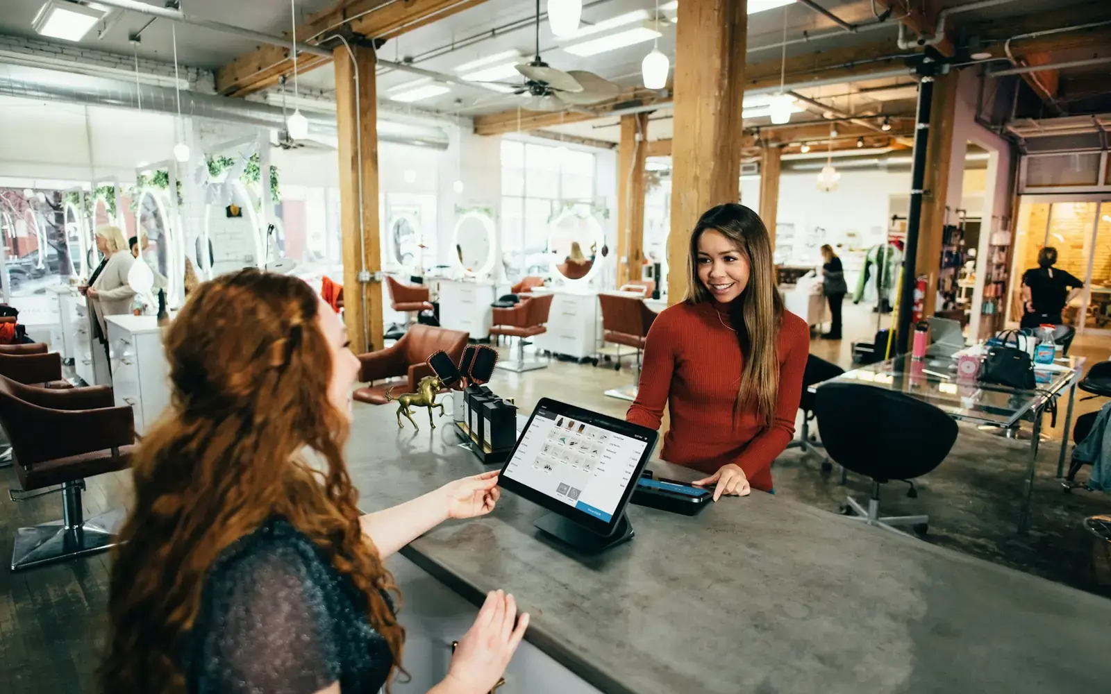 A salon owner at the front desk showing a client a tablet
