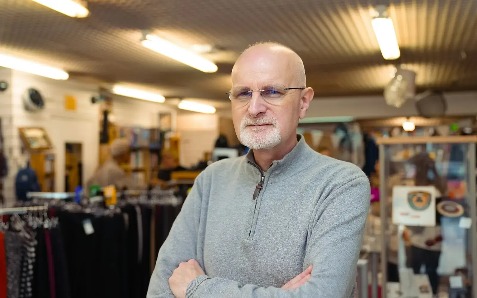 A shop owner with his arms folded, standing in his store