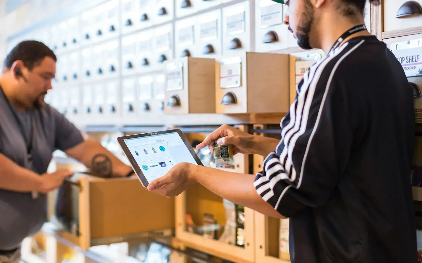 Two people in a stockroom, one holding a tablet out to show the other