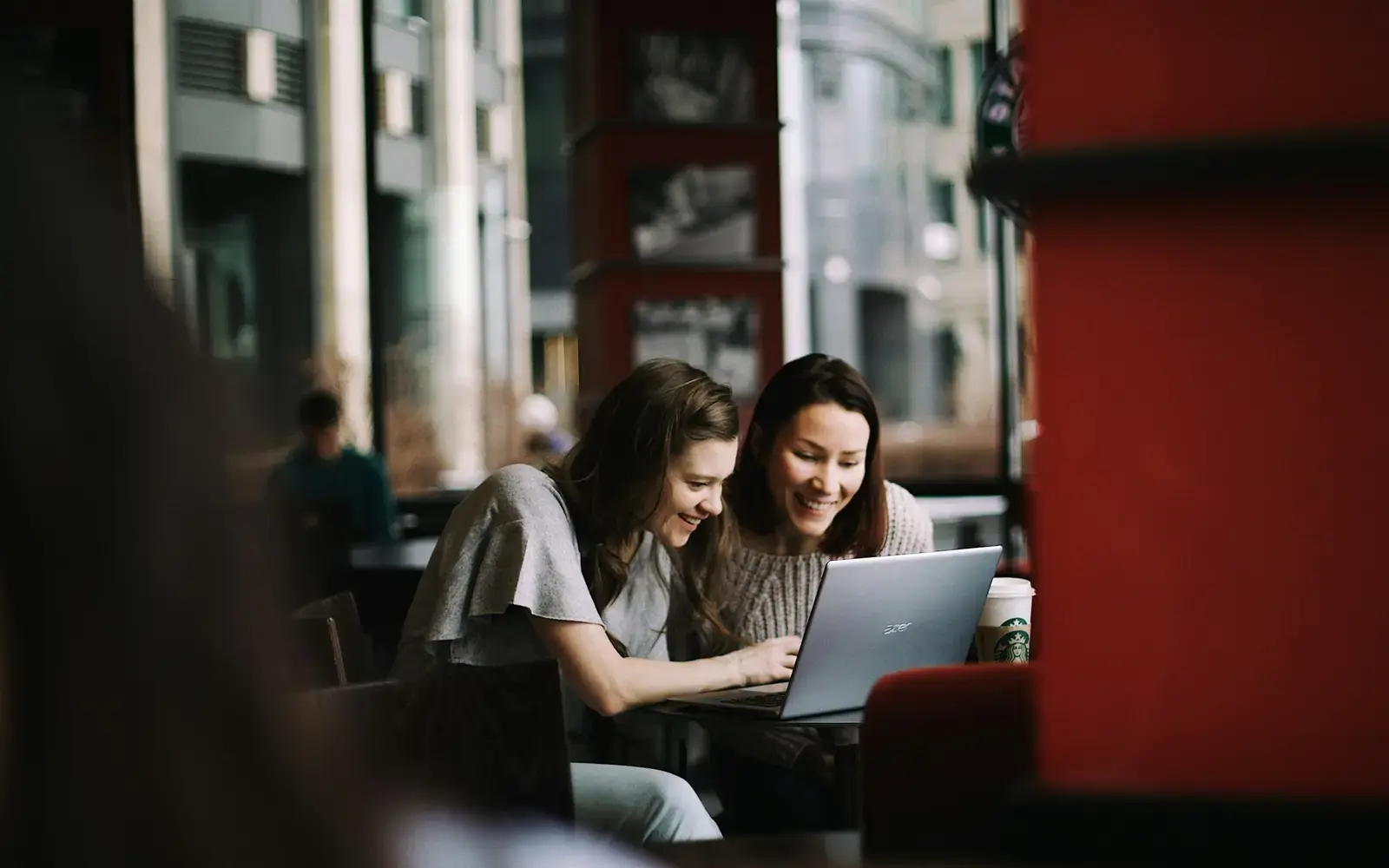 Two women sharing a laptop at a table in a cafe